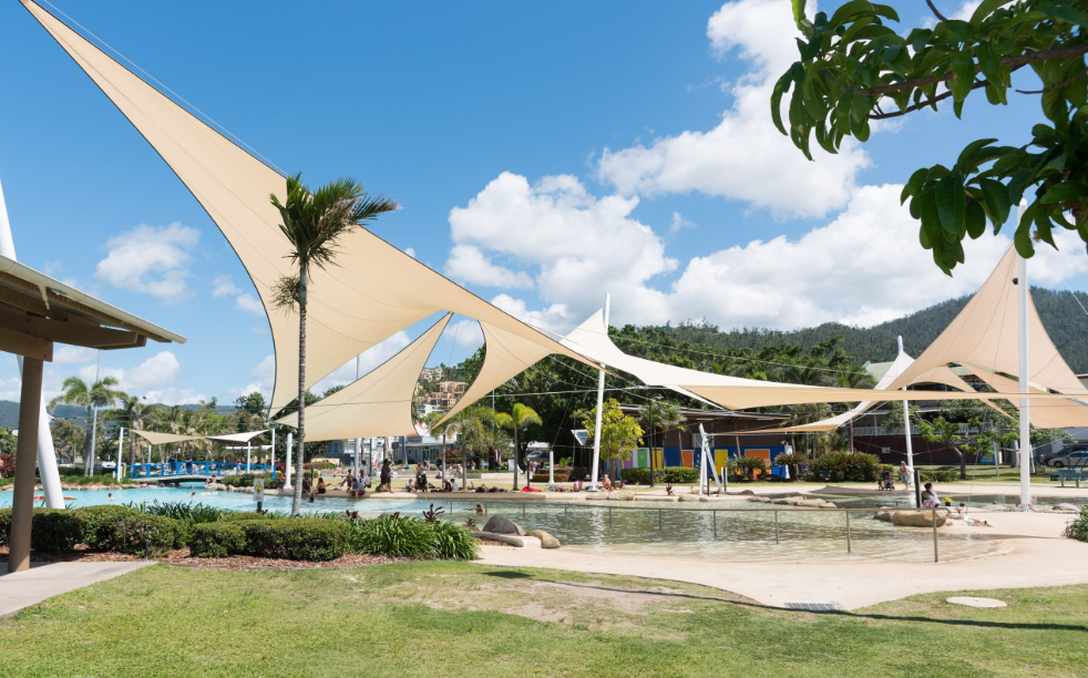 Colourful shade sail providing UV protection over a poolside lounge area